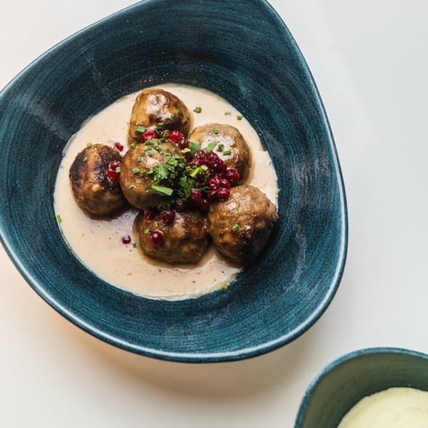 Waxin's Swedish meatballs in cream sauce, topped with lingonberries and chives, in a blue bowl.
