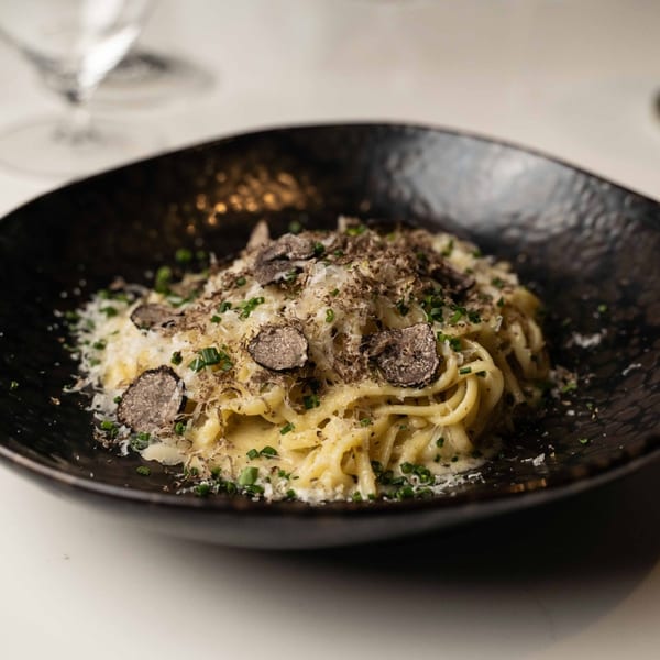 Waxin's truffle pasta, topped with shaved truffles, grated cheese, and chives in a black bowl.
