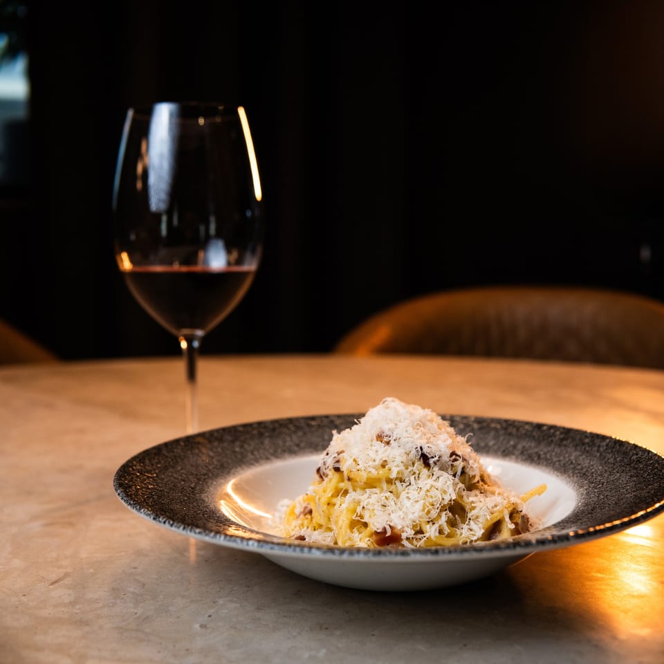 A plate of Waxin's pasta with grated cheese and a glass of red wine on a table.