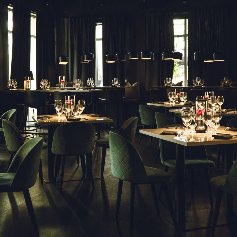 Dark, elegant dining room at Waxin's with green chairs, set tables, and modern pendant lights.