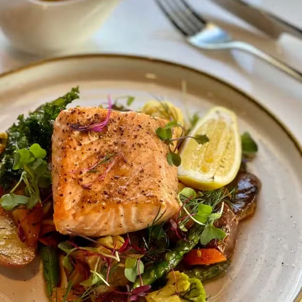 Pan-seared salmon with roasted vegetables, kale, and a lemon wedge on a white plate.