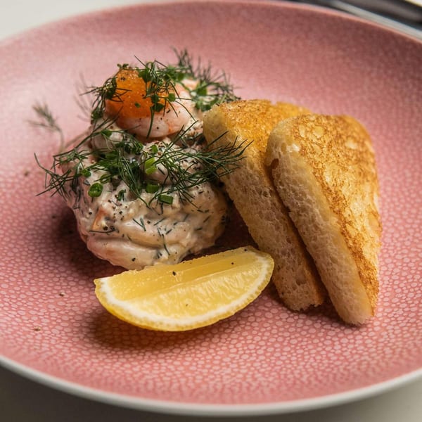 Shrimp skagen with dill, roe, and lemon, served with toasted bread on a pink plate.