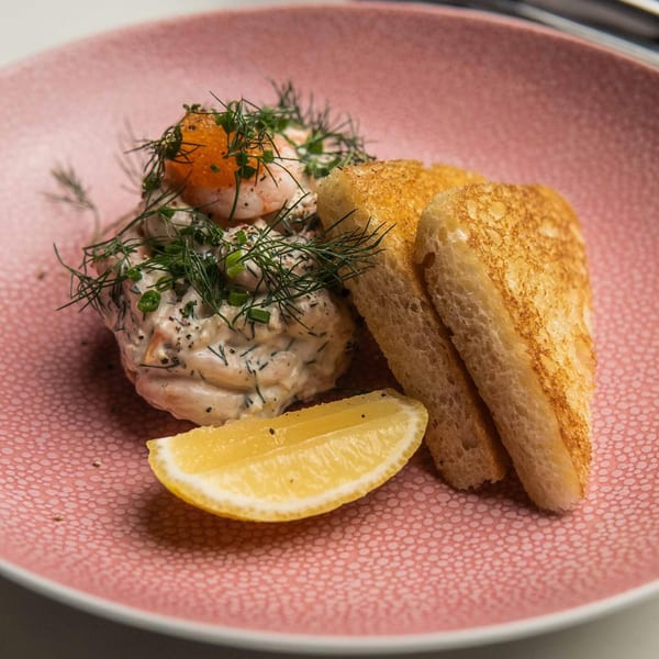 Shrimp skagen with dill, roe, and a lemon wedge, served with toasted bread on a pink plate.