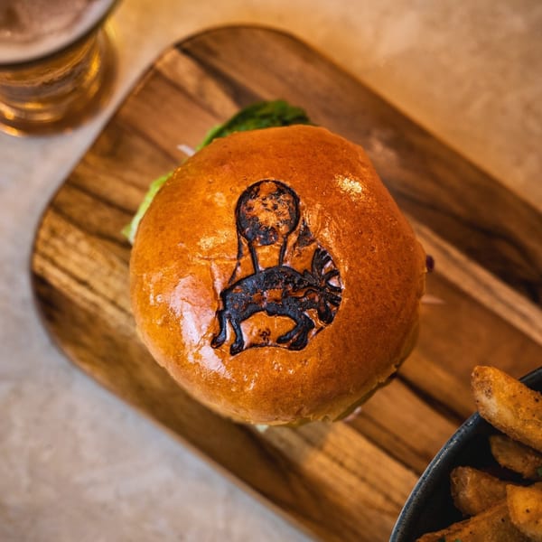 Waxin's burger with a branded bun, served with fries and a drink on a wooden board.