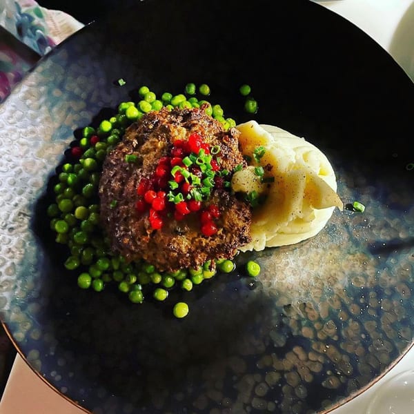 Waxin's meatloaf with mashed potatoes, green peas, red berries, and chives on a dark plate.