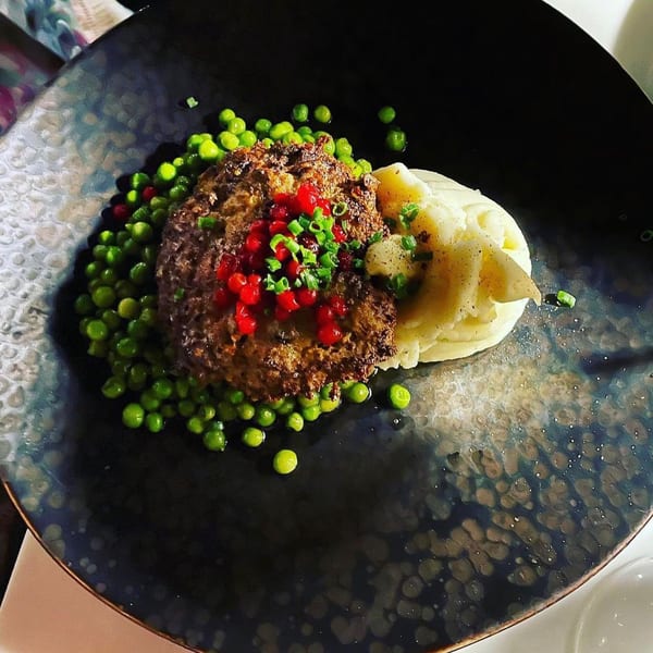 Meatloaf with red berries, green peas, and mashed potatoes on a dark, textured plate at Waxin's.