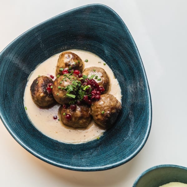 Waxin's Swedish meatballs in cream sauce, topped with lingonberries and chives, served in a blue bowl.